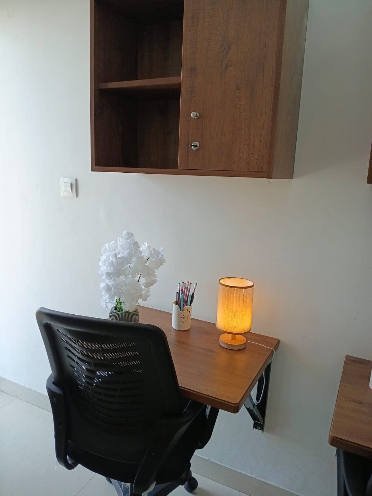 Minimalist home office featuring a wall-mounted wooden desk, black chair, and warm glowing lamp.